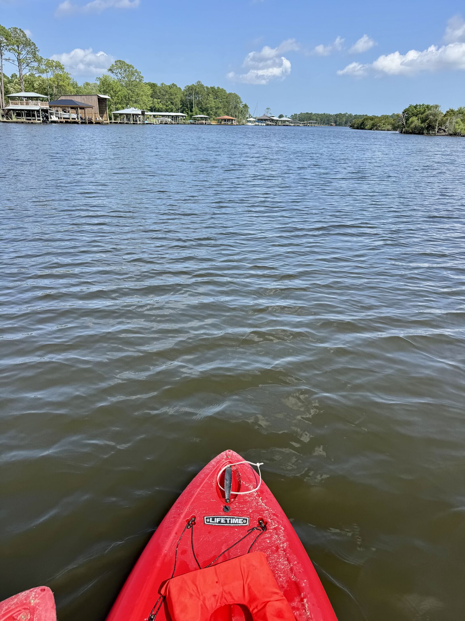 A calm body of water with a red kayak in the foreground and a dock with buildings in the background.