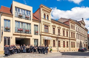 A hotel with a group of people in front, a street view, and a building with a sign that reads 'Hotel'. - Altmark Schwarzer Adler (Stendal)