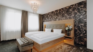 Una habitación de hotel con una cama grande, un cabecero de madera, una mesita de noche con un florero y una araña.