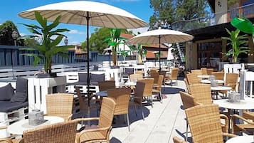 Ein Außenbereich mit Korbmöbeln, Tischen, Sonnenschirmen und Blumentöpfen.