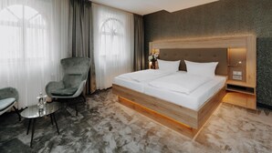 Una habitación de hotel con una cama grande, una silla, una mesita y una mesita de noche con una lámpara.