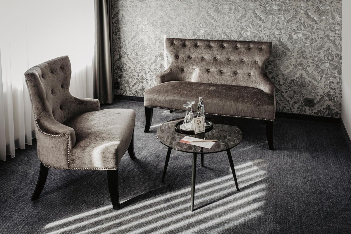 A room with a tufted sofa, a cushioned armchair, and a small round table with a glass top.