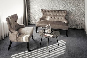 A room with a tufted sofa, a cushioned armchair, and a round coffee table with a decorative item on it. - Altmark Schwarzer Adler (Stendal)