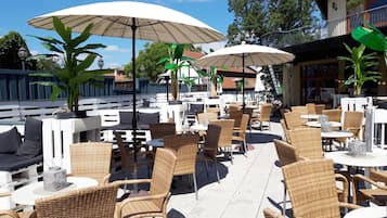 Ein Café mit Außenbereich, Korbmöbeln, weißen Tischen und großen Sonnenschirmen.