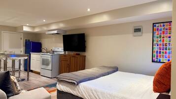 A compact room with a bed, a kitchenette, a dining area, and a wall-mounted TV.