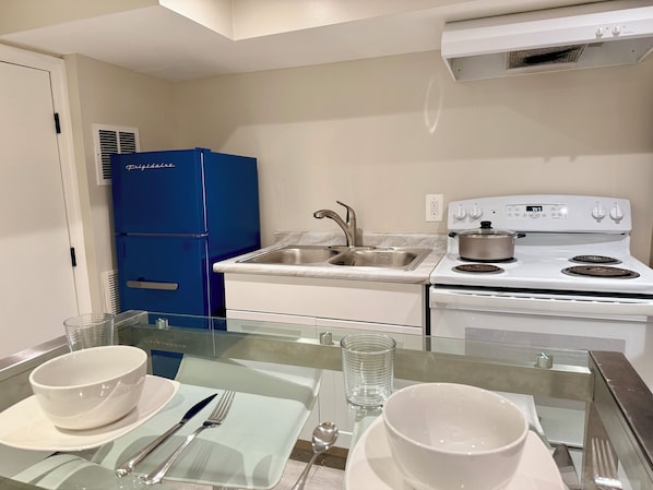 A modern kitchen with a blue refrigerator, white stove, and a glass dining table set with white dishes and cutlery.