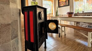 A rustic kitchen with a wood-burning stove, stone walls, and a wooden ceiling.