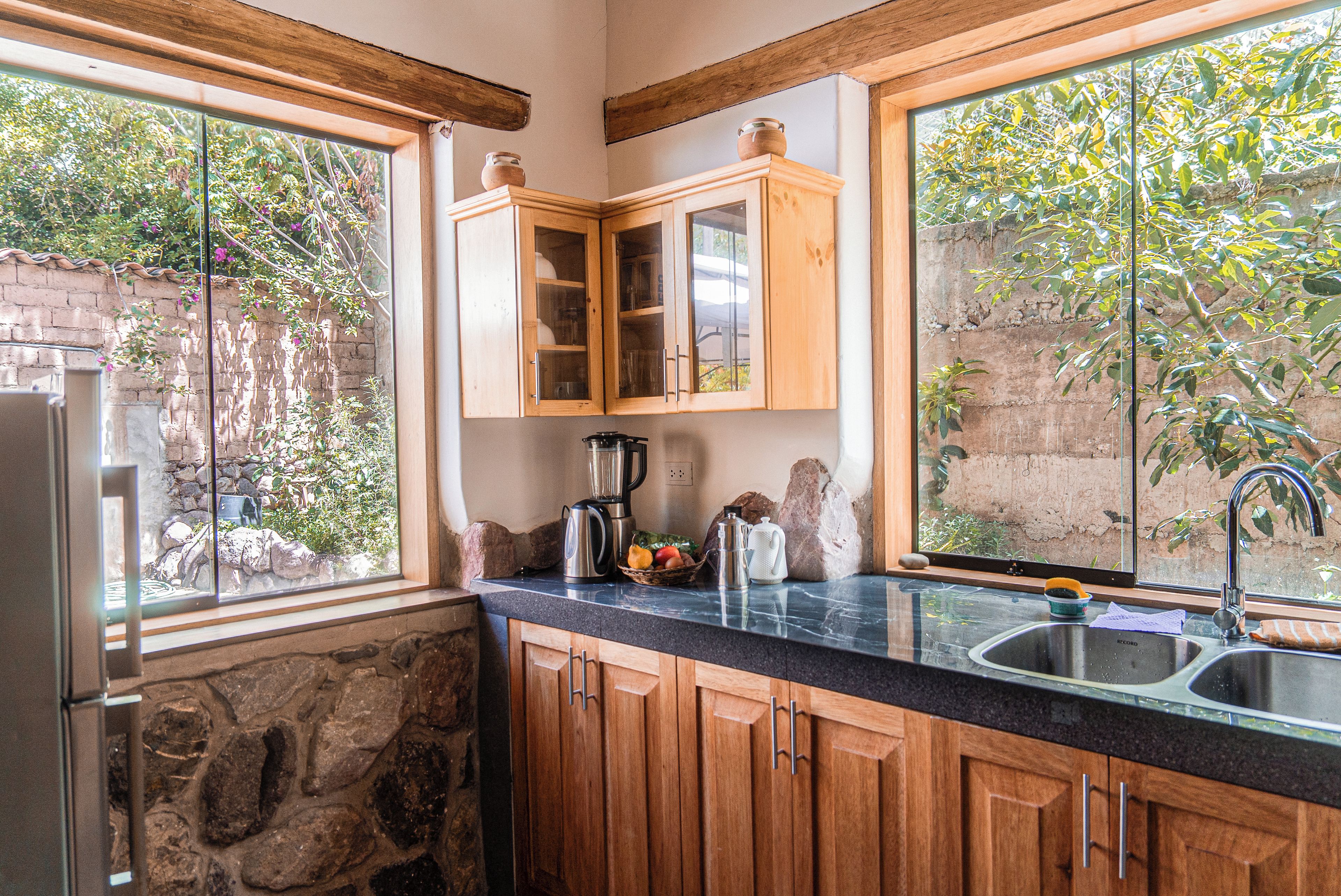 A kitchen with wooden cabinets, a stone wall, and a view of greenery outside.