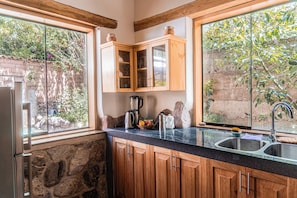 A kitchen with wooden cabinets, a stone wall, and a view of greenery outside.