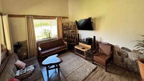 A cozy living room with a wooden ceiling, a flat-screen TV mounted on the wall, a sofa, a coffee table, and a stone accent wall.
