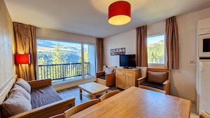 A room with a balcony, a TV, a dining table, and a sofa.