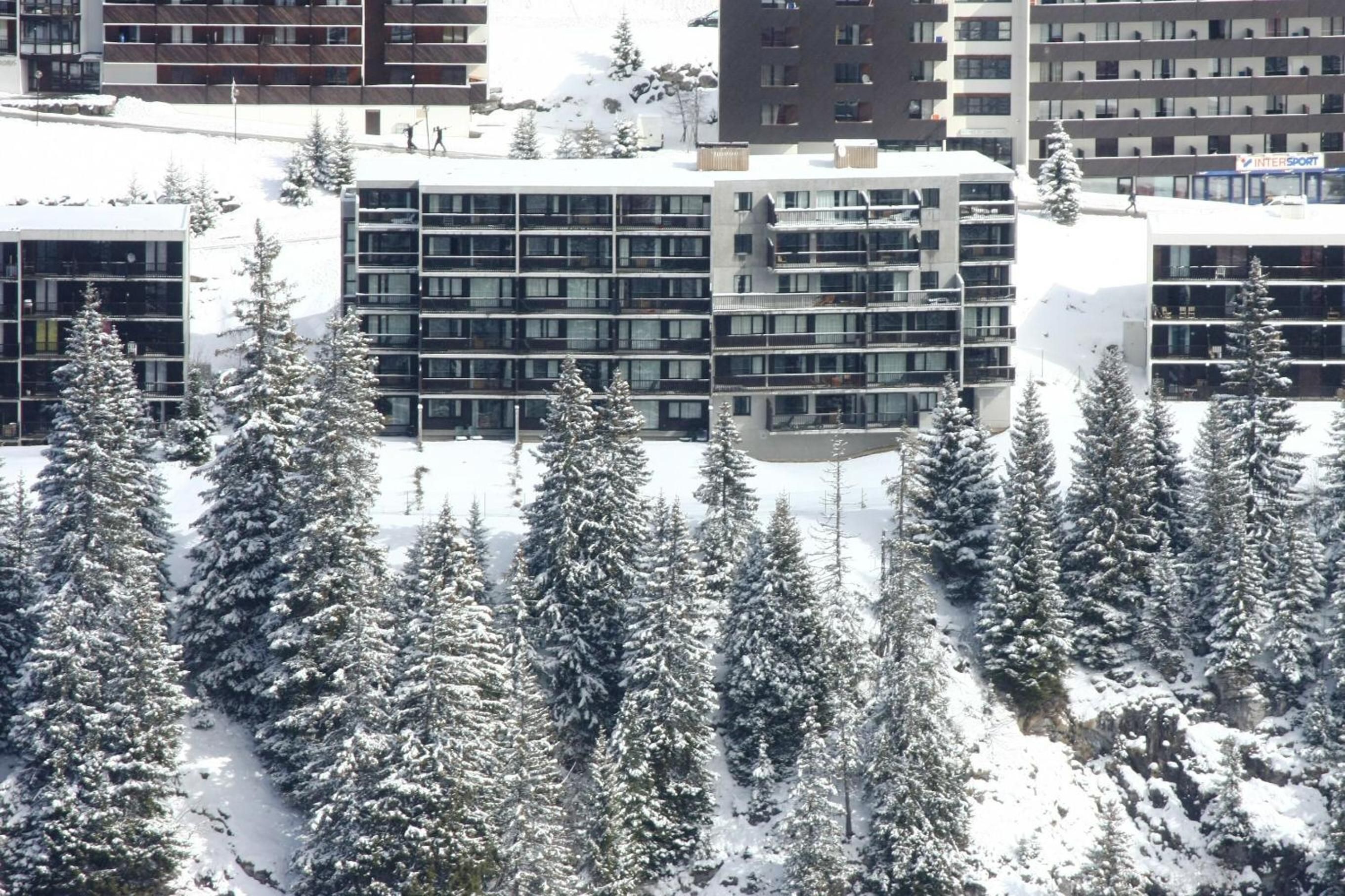 A modern building with multiple floors, surrounded by snow-covered trees.