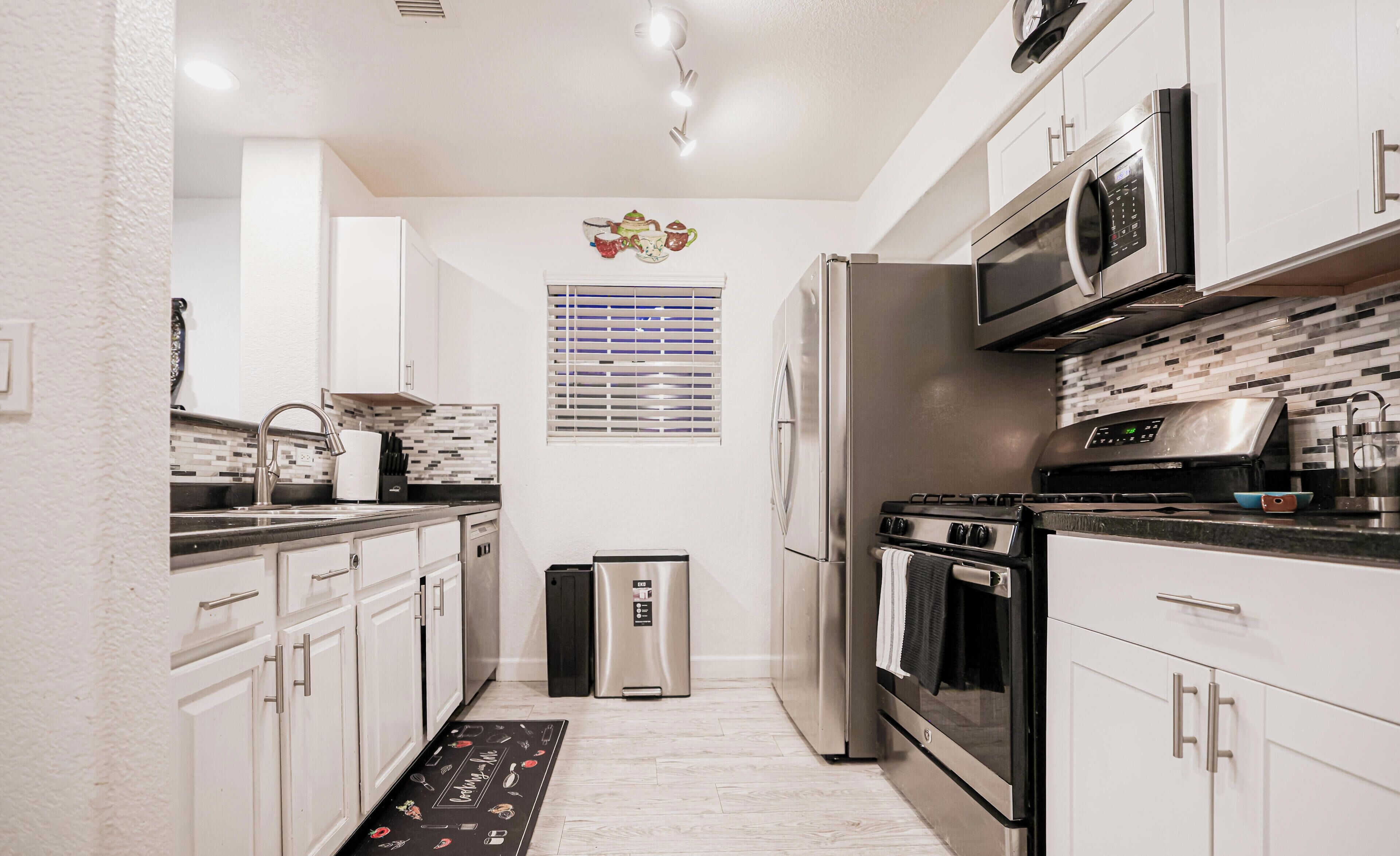 A modern kitchen with stainless steel appliances, white cabinetry, and a black countertop.
