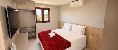 Un dormitorio con cama, televisión, ventana y aire acondicionado.