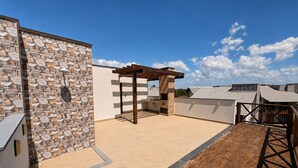 Una terraza en la azotea con muro de piedra, pérgola y zona de barbacoa.