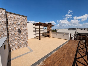Una terraza en la azotea con muro de piedra, pérgola y zona de barbacoa.