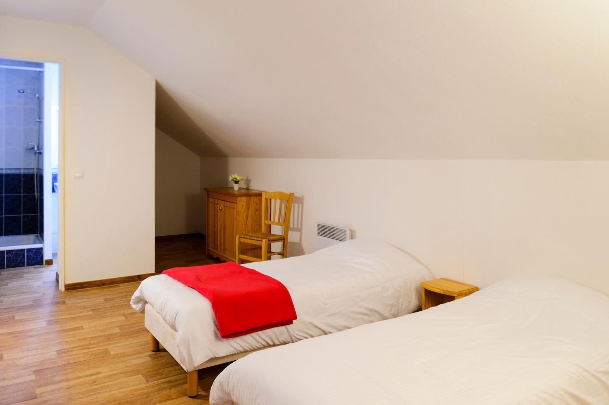 Une chambre avec deux lits, une armoire en bois, une chaise et un radiateur.