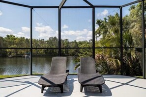 A covered outdoor seating area with two chairs, a view of a lake, and surrounding greenery. - Crystal River Waterfront w/ Dock, Pool & Manatees! (Crystal River)