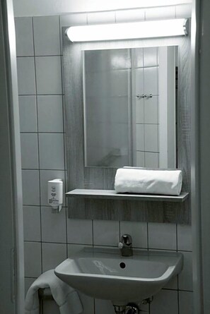Une salle de bain avec un lavabo blanc, un miroir et une serviette posée sur une étagère.