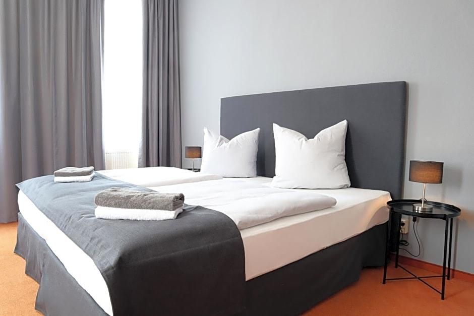 Habitación de hotel con una cama grande, dos mesitas de noche, una lámpara y una ventana con cortinas.