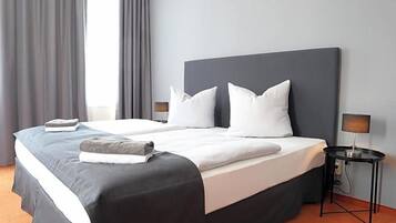 Ein Hotelzimmer mit einem großen Bett, zwei Nachttischen, einer Lampe und einem Fenster mit Vorhängen.