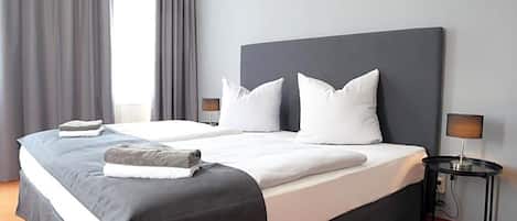 A hotel room with a large bed, two bedside tables, a lamp, and a window with curtains.