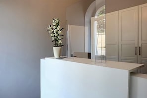 Un comptoir d’accueil agrémenté d’une plante en pot, une cloison en verre et une vue sur une porte donnant sur une pièce elle-même dotée d’une porte en verre.