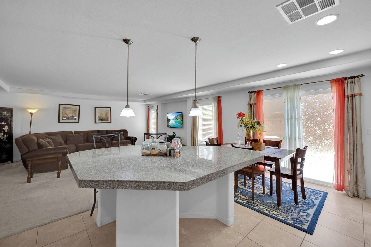 Una cocina moderna con una isla central, comedor con sillas, un sofá y un televisor en la pared.