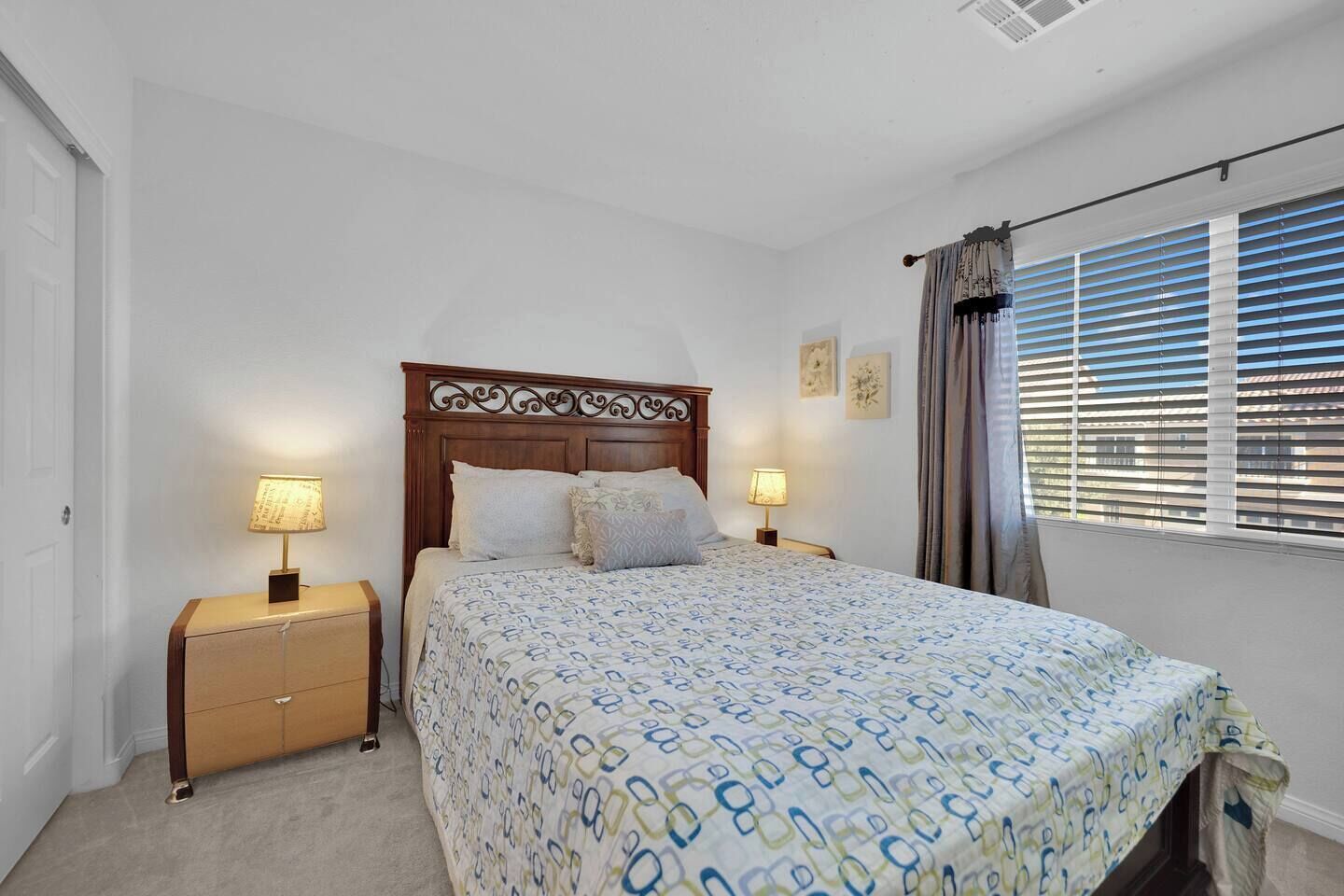 Une chambre à coucher comprenant un lit, deux tables de chevet, une commode, une fenêtre avec des stores et une porte.