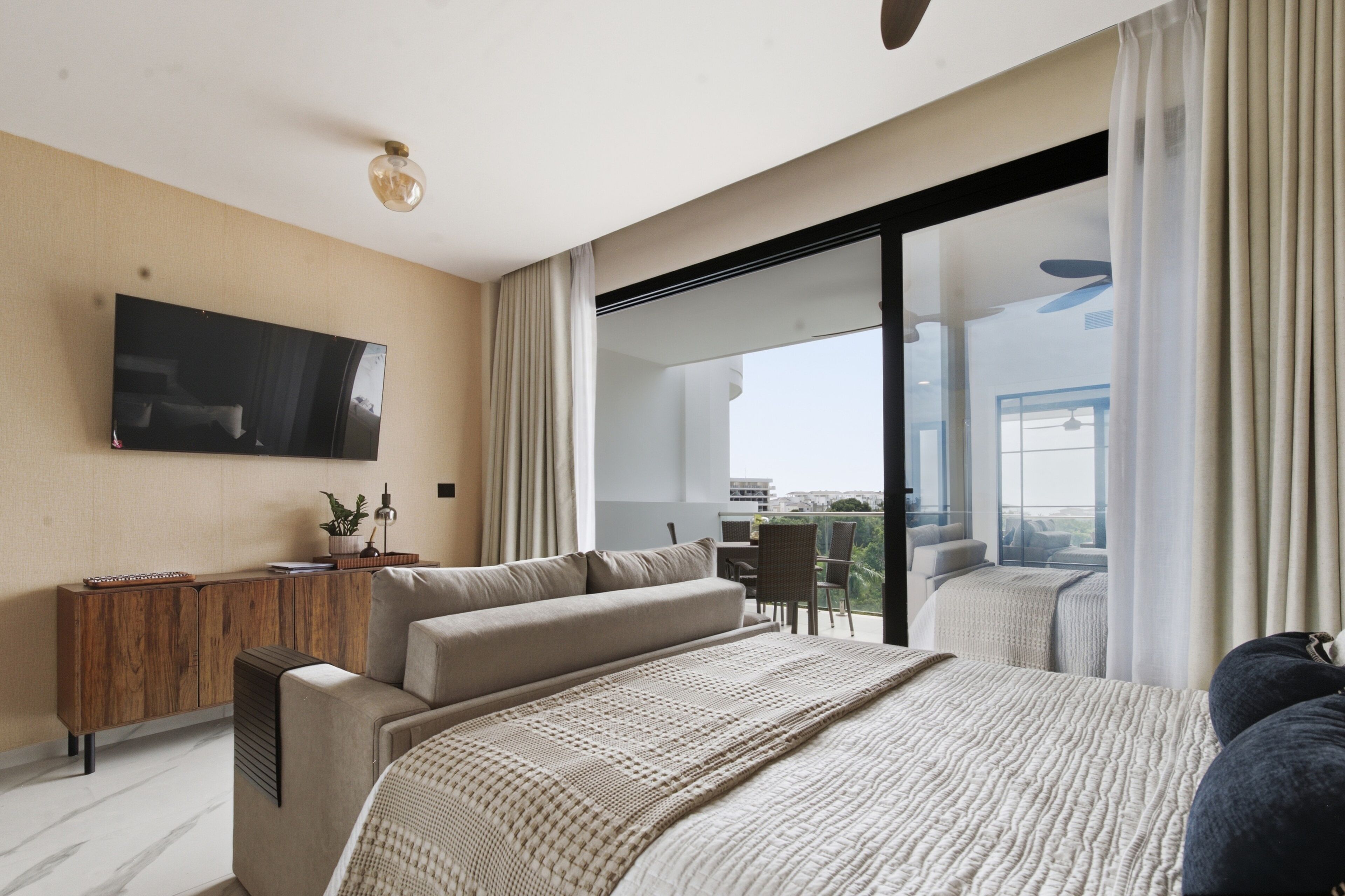 Ein modernes Hotelzimmer mit einem großen Bett, einem flachbildfernseher an der Wand, einem Holztischchen und einem Balkon mit Sitzgelegenheit.