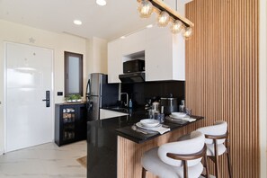 A modern kitchen with a black countertop, stainless steel appliances, and a wooden accent wall. - Luxury Golf View Studio/Elegance&Serenity Infinity Pool (Bavaro)