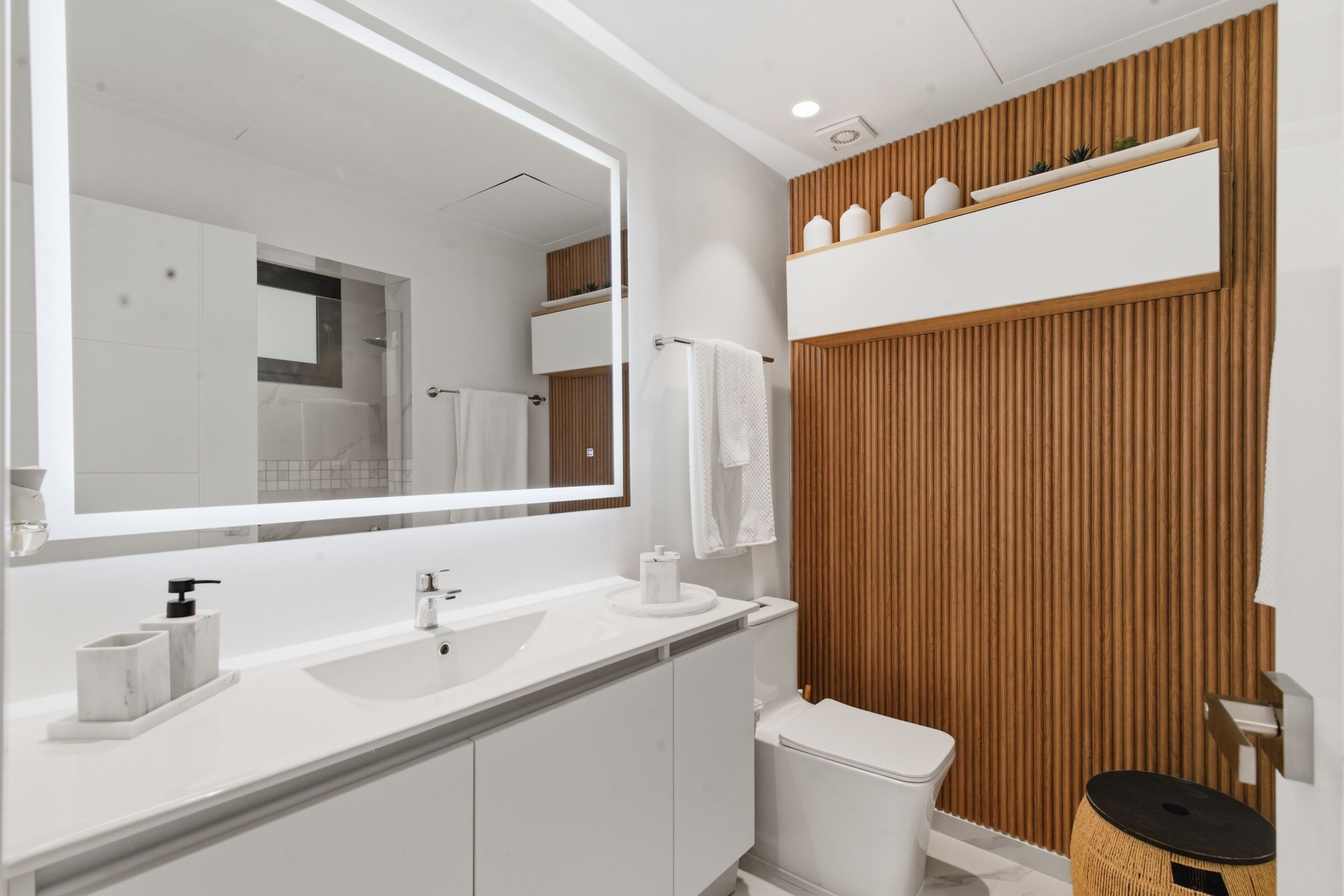 A modern bathroom with a large mirror, white fixtures, and wooden paneling.