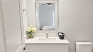A bathroom with a white vanity, a mirror, a toilet, and a ceiling fan. - Work • Play • Stay  3 Min to Stadium • Near Job Sites, Shopping & Dining (Port Charlotte)