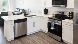 A modern kitchen with white cabinetry, stainless steel appliances, and a wooden floor. - Work • Play • Stay  3 Min to Stadium • Near Job Sites, Shopping & Dining (Port Charlotte)
