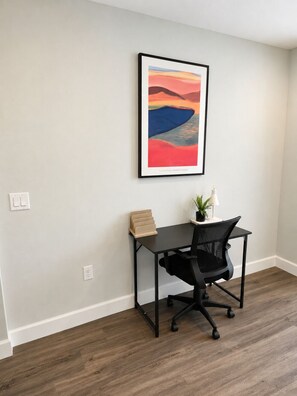 A room with a desk, chair, and a framed painting on the wall.
