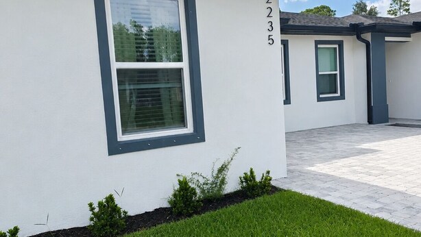 A modern building with a white facade, numbered 2235, featuring a large window and a small garden area with grass and shrubs. - Work • Play • Stay  3 Min to Stadium • Near Job Sites, Shopping & Dining (Port Charlotte)