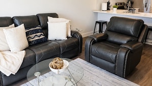 A modern living room with a leather sofa, a glass coffee table, and a patterned rug. - Work • Play • Stay  3 Min to Stadium • Near Job Sites, Shopping & Dining (Port Charlotte)