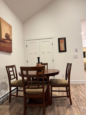 A dining area with a round table and four wooden chairs, white walls, and a door with a picture frame.