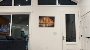 A modern interior with a large window, a painting of a sunset, and a door leading to a room.