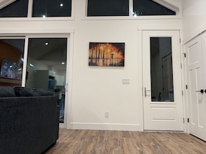A modern interior with a large window, a painting of a sunset, and a door leading to a room.