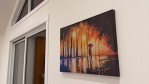 A room with a large window, a painting of a rainy scene, and a white wall.