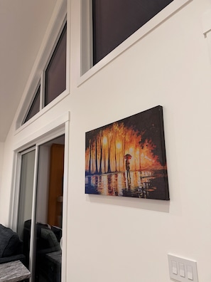 A room with a large window, a painting of a rainy scene, and a white wall.