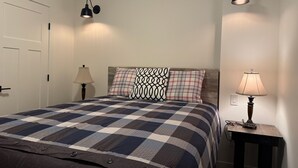 A bedroom with a checkered bedspread, two bedside lamps, and a nightstand with a lamp.