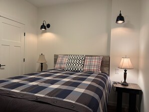 A bedroom with a checkered bedspread, two bedside lamps, and a nightstand with a lamp.