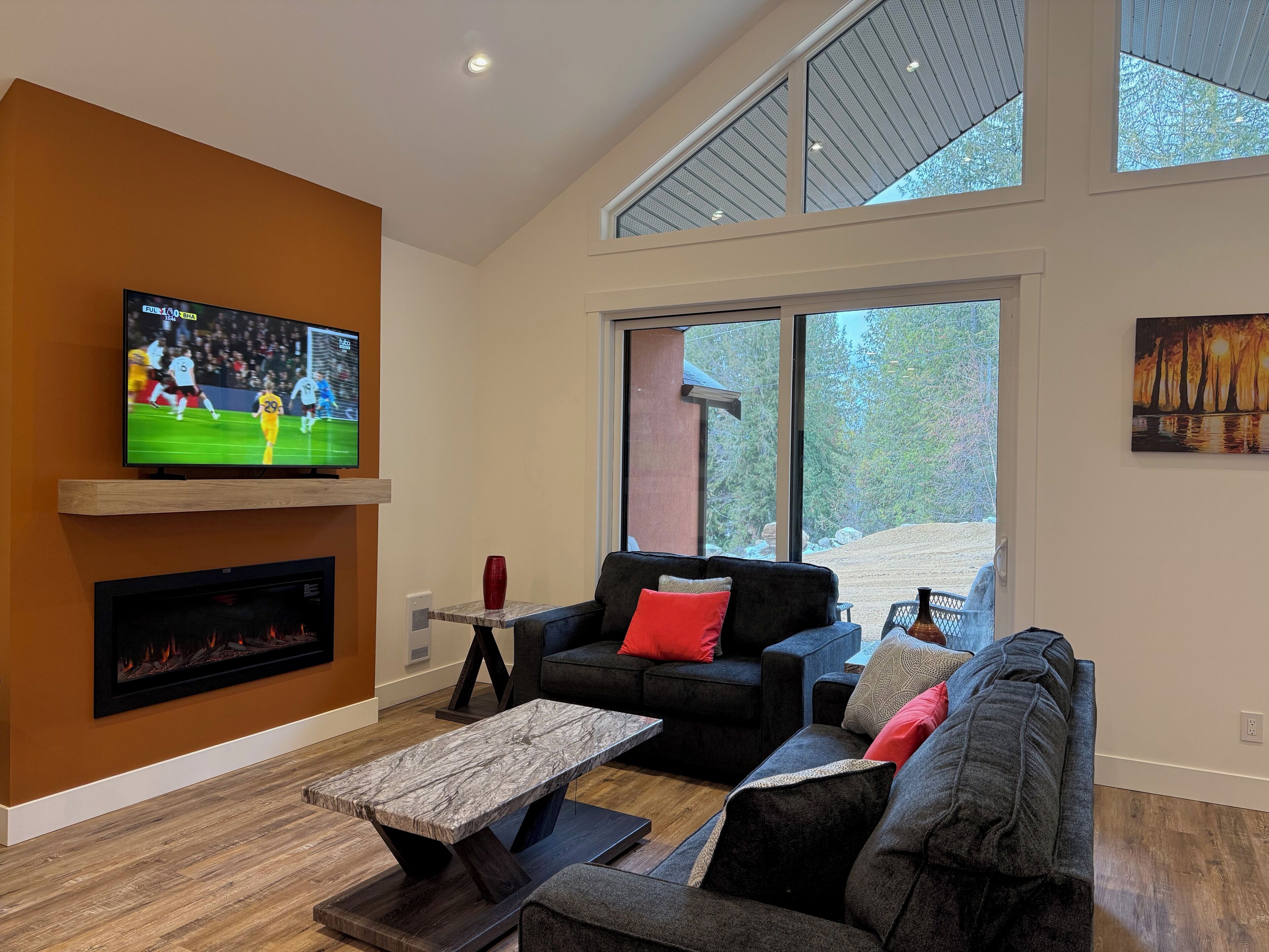 A modern living room with a fireplace, a television, and a large window offering a view of the outdoors.