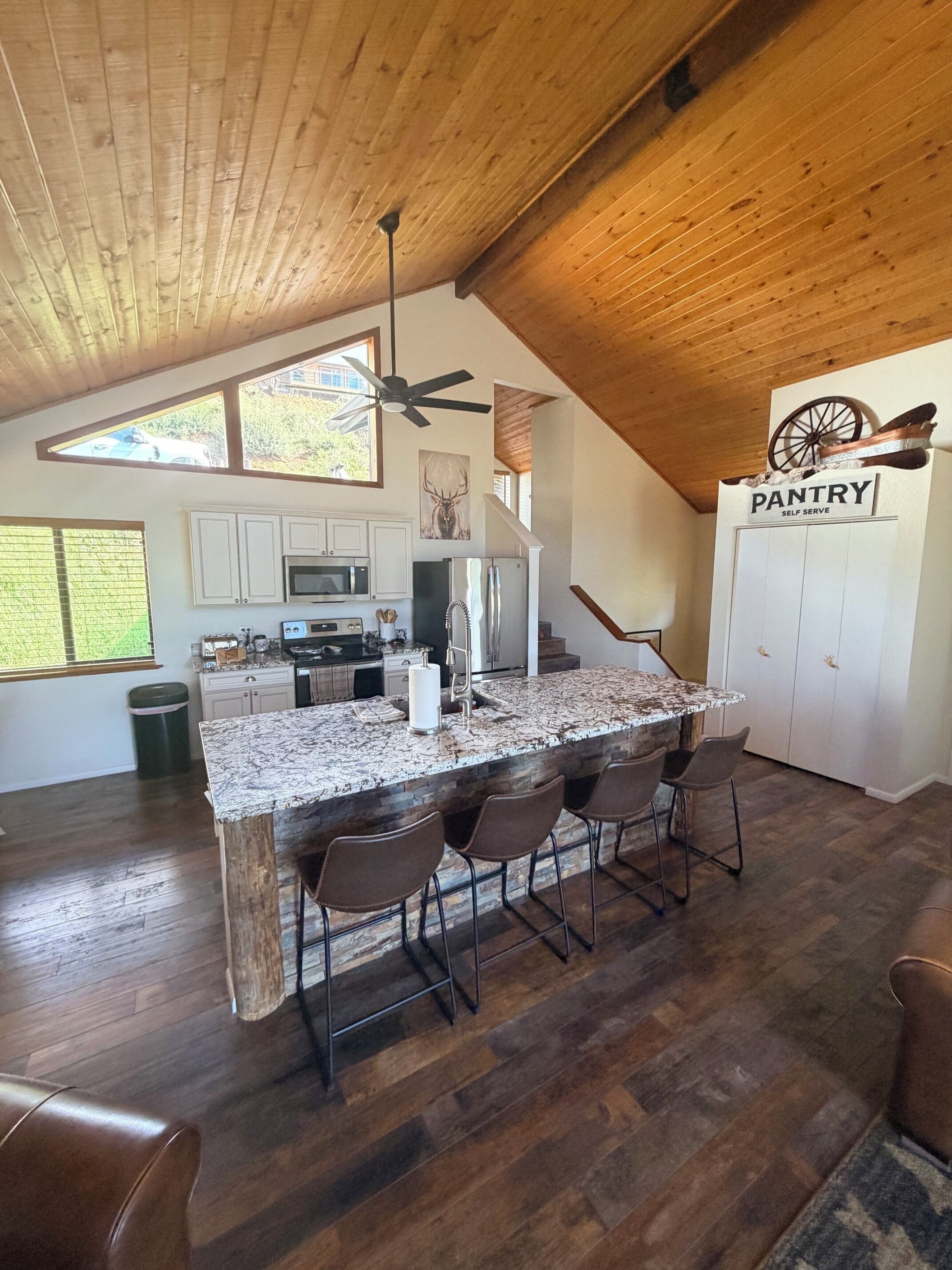 A kitchen with a granite countertop, bar stools, and a ceiling fan.