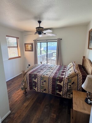 A bedroom with a bed, a ceiling fan, a window with blinds, a door leading to a balcony, and a painting on the wall. - 3-bedroom cabin in charming Pine with cozy mountain vibes and AMAZING views (Pine)