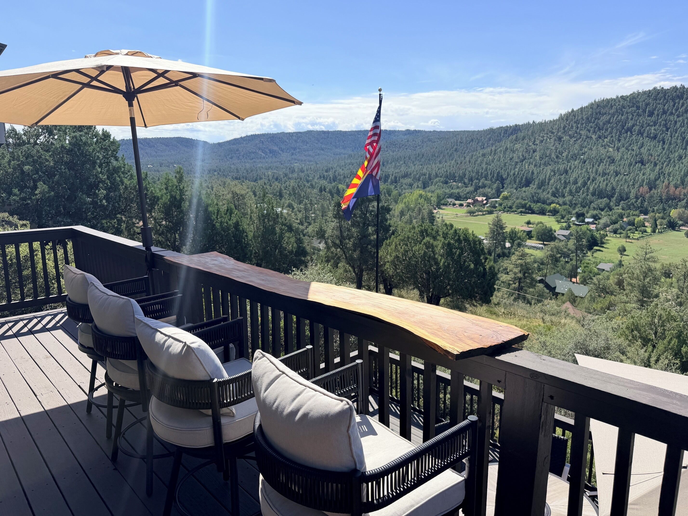 A deck with outdoor furniture and a flag, overlooking a forested valley.