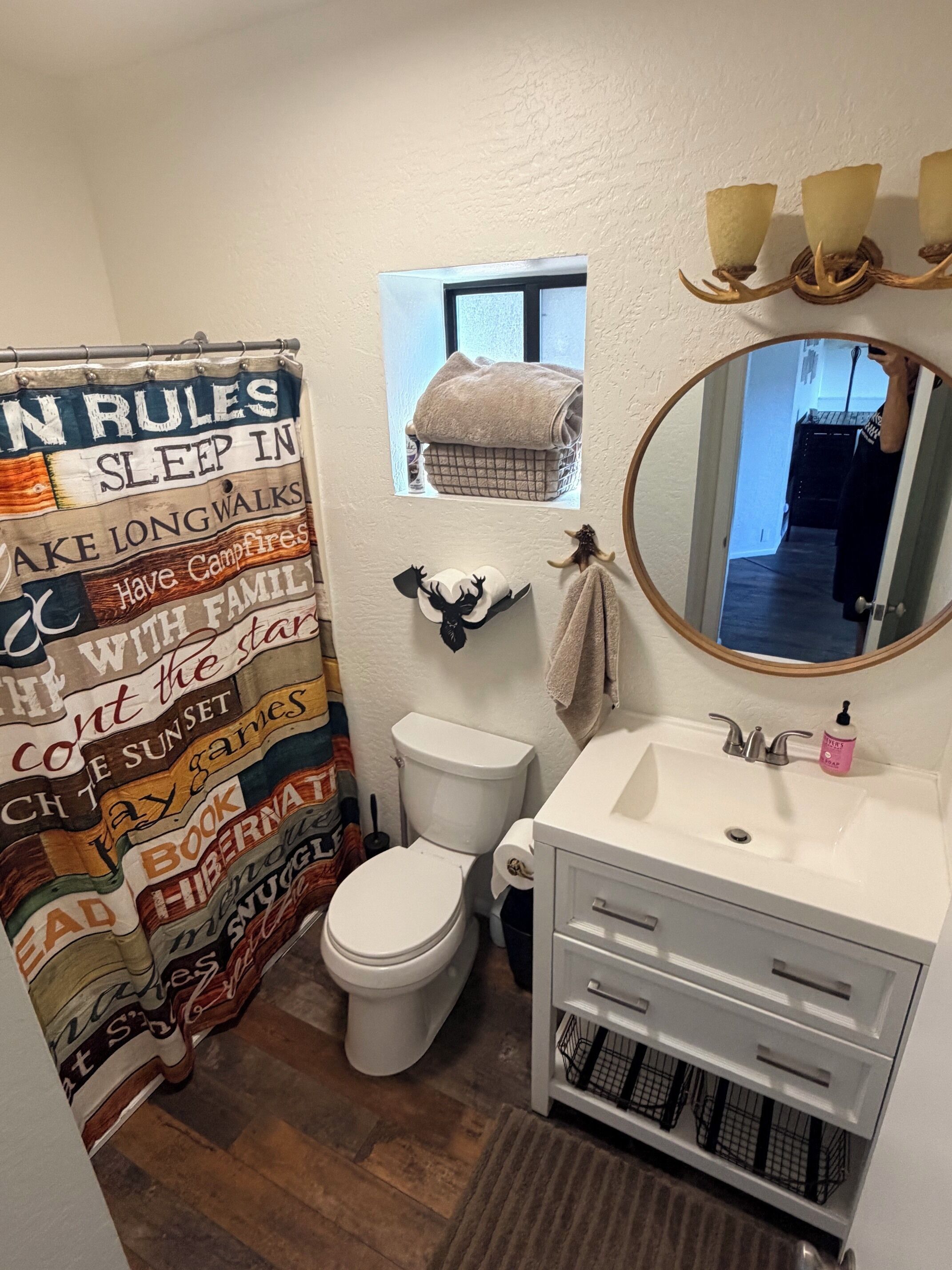 Ein Badezimmer mit Duschvorhang, Toilette, Waschbecken mit Spiegel und einem Fenster über der Toilette.