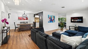 Uma sala de estar moderna com sofá, área de jantar com mesa e cadeiras, e televisão fixada na parede.